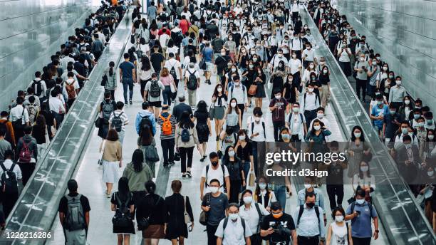 crowd of busy commuters with protective face mask walking through platforms at subway station during office peak hours in the city - crowd masks stock pictures, royalty-free photos & images