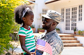 African American male soldier holding his daughter with a US flag in his arms