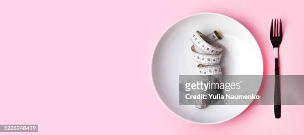 dieting and health care concept. plate and cutlery with measuring tape. measure tape on white plate, pink background. flat lay and copy space for text. the concept of harmony and weight loss after self-isolation. - fasten stock-fotos und bilder