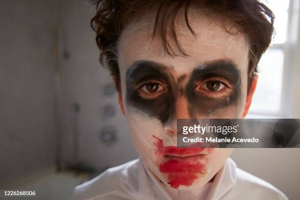 young boy with brown curly hair brown eyes wearing halloween make up close up to the camera face to face with camera selective focus window sill behind him messy curly hair costume makeup - kinder schminken stockfoto's en -beelden