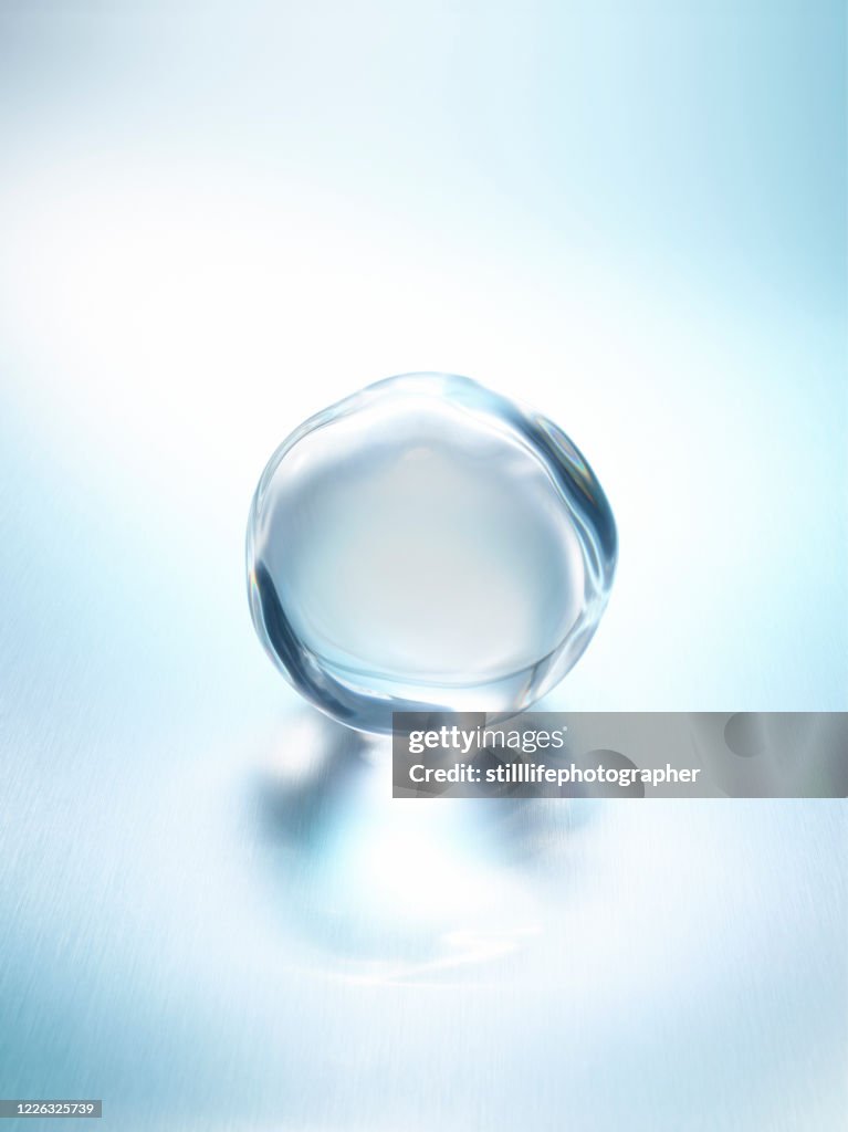 Close up view in a 45 degree angle of a shining clear water droplet on a light blue metallic surface with reflection