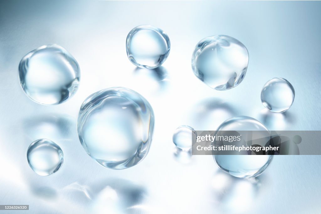 A group of large clear water droplets against blue metallic surface with reflections, close up view in a 45 degree angle