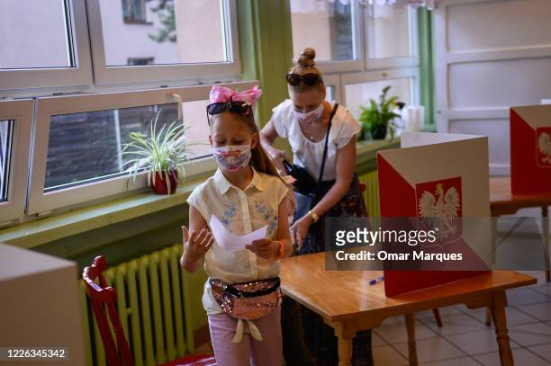 Girl wears a protective face mask as she walks towards the ballot box with her mother's vote during Poland's Presidential elections runoff on July...
