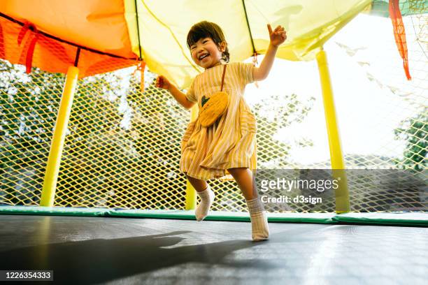 joyful little asian toddler girl smiling happily and having fun jumping in a bouncy castle in a outdoor playground - angelica hale fotografías e imágenes de stock