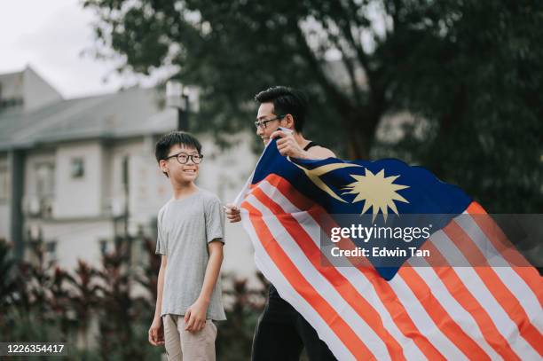 un cinese asiatico indossare e avvolgere suo figlio con bandiera malesia nel parco pubblico - malaysia independence day foto e immagini stock