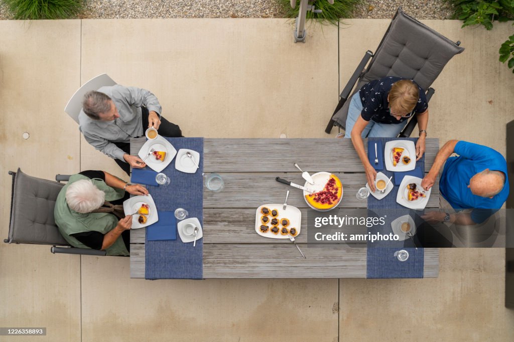 Seniors enjoying afternoon coffee in garden on long table view from above