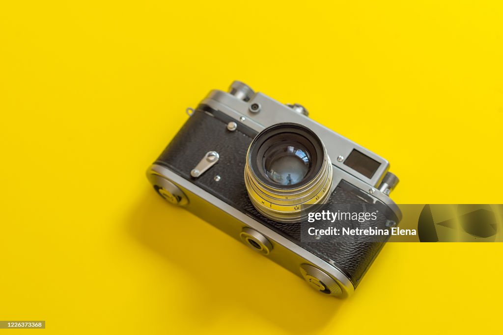Retro, vintage film camera on a yellow colorful fashionable modern background. Camera lens with reflections. Film camera