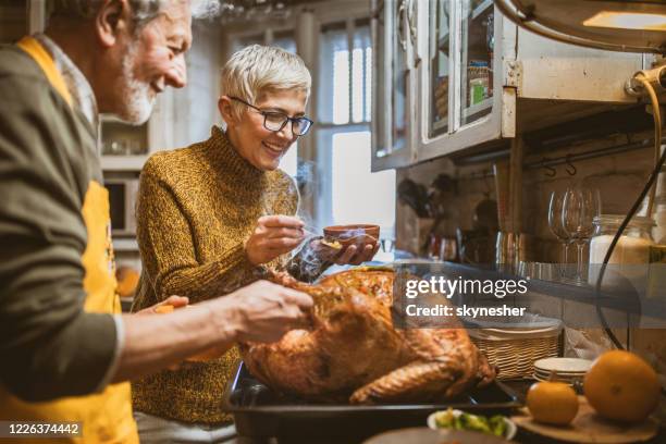 glückliches senior-paar schmückt truthahn am thanksgiving-tag. - geröstet stock-fotos und bilder