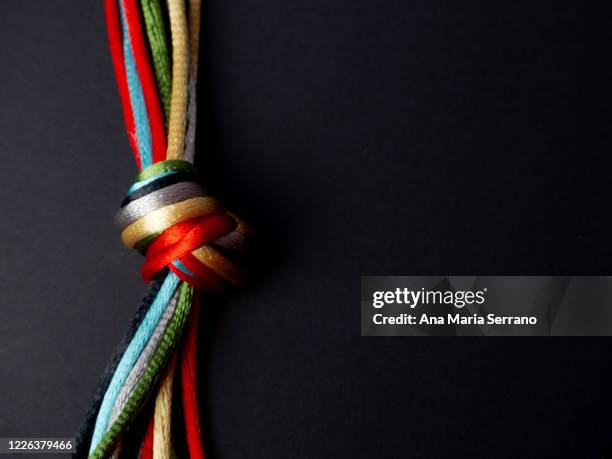 a knot with many twine of different colors on a black background - tied knot stock pictures, royalty-free photos & images