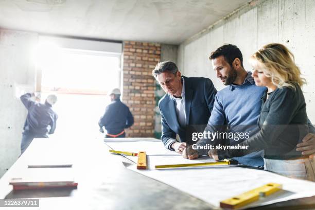 young couple and their agent examining blueprints at construction site. - trabalho de design imagens e fotografias de stock