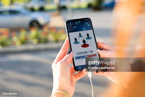 woman holding a phone in the street using the contact tracing app - state of emergency stock pictures, royalty-free photos & images