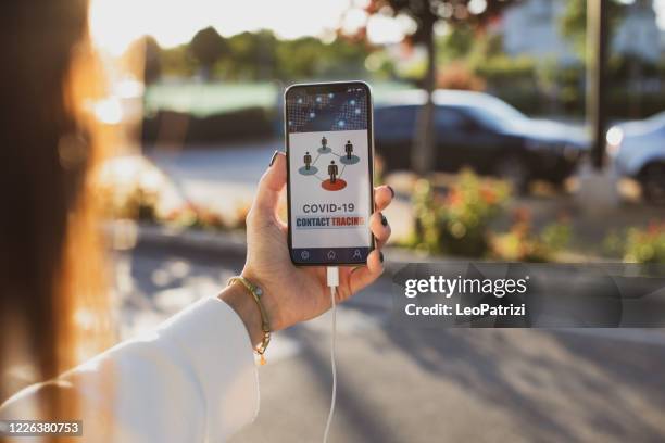 woman holding a phone in the street using the contact tracing app - contact tracing stock pictures, royalty-free photos & images