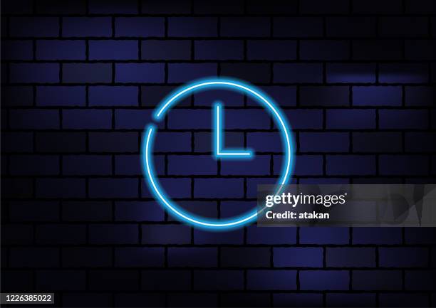 clock icon blue neon light on dark brick wall. - clock on wall stock illustrations