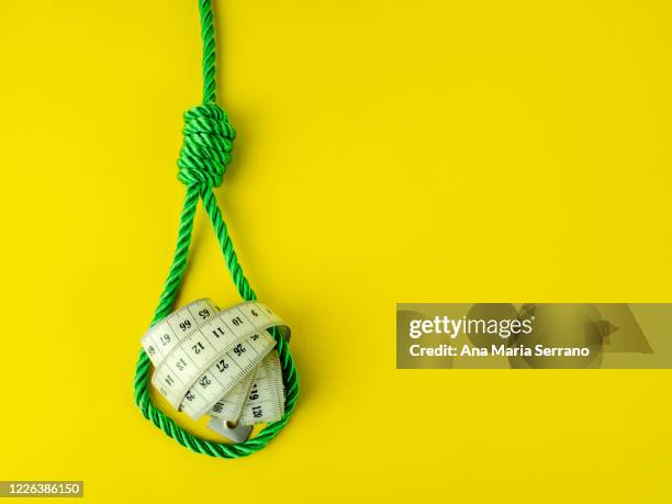 a hangman's knot and a tape measure on a yellow background. eating disorder concept - hanging gallows stock pictures, royalty-free photos & images