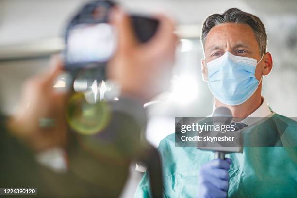 männlicher arzt gibt ein interview vor der kamera im krankenhaus. - medical news stock-fotos und bilder