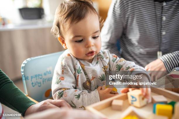 baby boy and his parents playing with toy blocks on table at home - high chair stock pictures, royalty-free photos & images