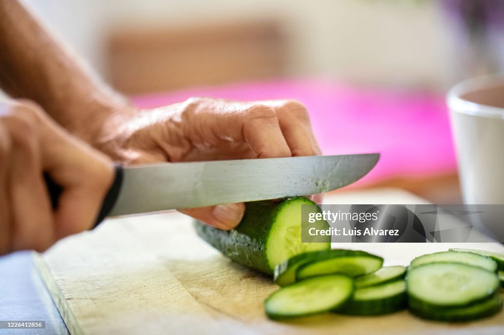 Hands of senior woman cutting cucumber on board