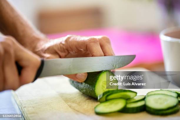 hands of senior woman cutting cucumber on board - cucumber imagens e fotografias de stock