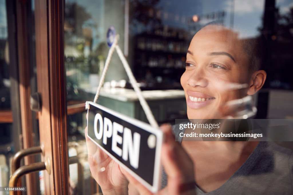 Female Owner Of Start Up Coffee Shop Or Restaurant Turning Round Open Sign On Door