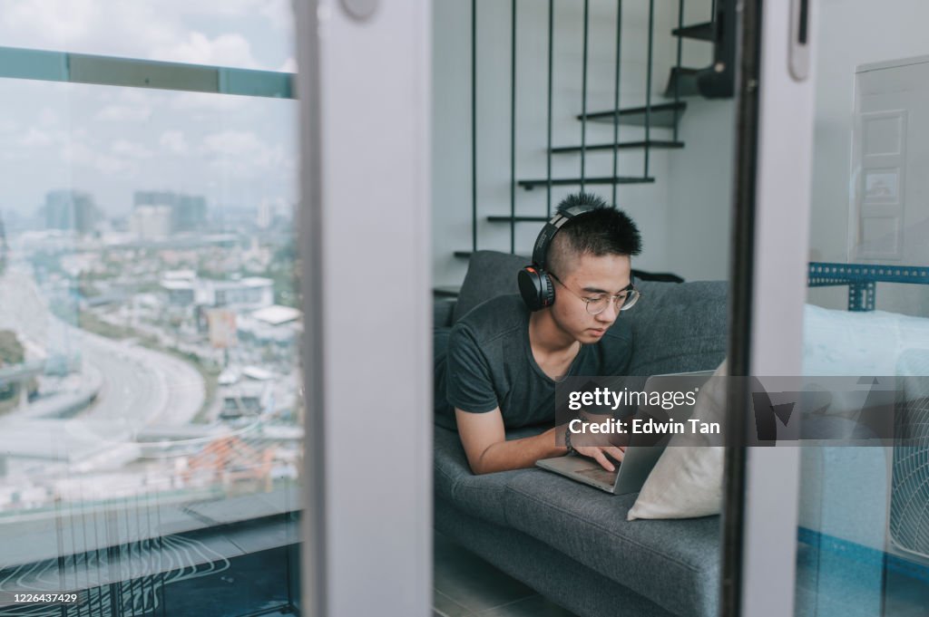 Um adolescente asiático escola em casa estudando em casa na sala de estar usando laptop