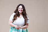Laughing happy plus size model in casual clothes, fat woman on beige background