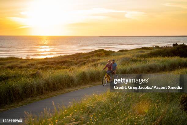 couple ride a tandem bicycle along a pathway at sunrise - tandem bicycle foto e immagini stock
