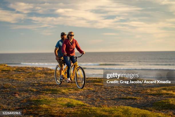 couple ride a tandem bicycle along a pathway at sunrise - bicycle tandem stock-fotos und bilder