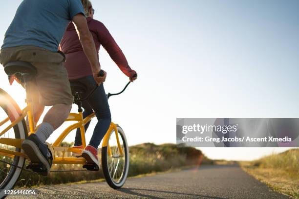 couple ride a tandem bicycle along a pathway at sunrise - tandem bicycle stock-fotos und bilder