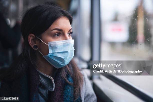 woman with protective face mask looking through the window. - coronavirus symptoms stock pictures, royalty-free photos & images