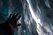 Hand reaching the ice inside a cave in Matanuska Glacier, Alaska. Looks like a person trapped, in distress, asking for help; confined, caught, imprisoned; all while walking, trekking on the snow.