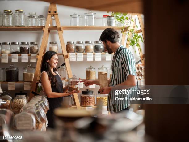 gelukkige spaanse werknemer die jonge mens in nul afvalopslag helpt - retail and consumer products stockfoto's en -beelden