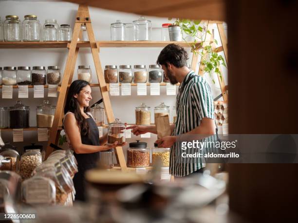 happy hispanic employee helping young man in zero waste store - retail place stock pictures, royalty-free photos & images
