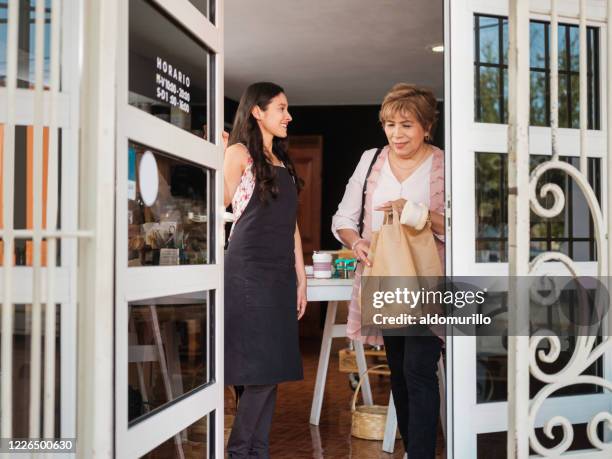 happy employee opening door for customer with paper bags - abrir a porta sair imagens e fotografias de stock