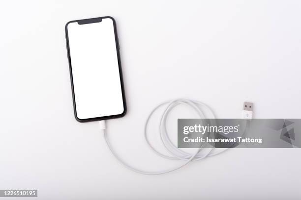 smartphone connects to charger through usb cable on white background top view - cargador de móvil fotografías e imágenes de stock