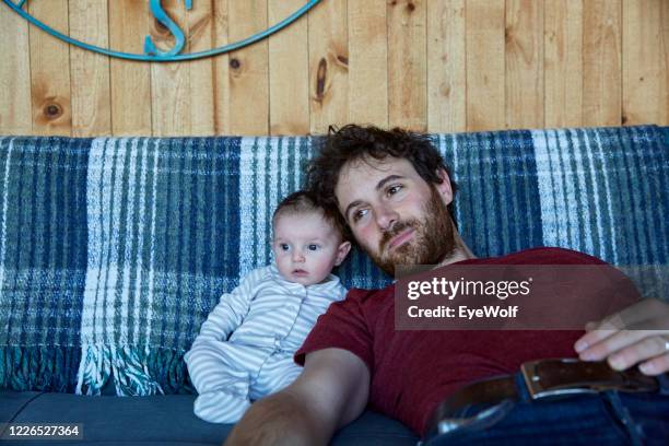a father and his baby daughter sitting on a couch together looking off camera. - bush baby fotografías e imágenes de stock