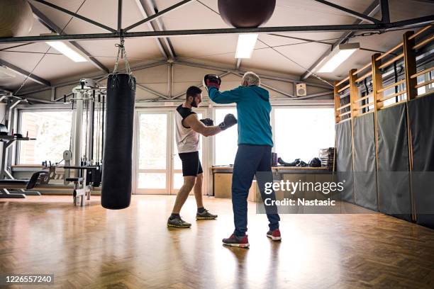 young boxer training with senior trainer in gym - boxing trainer stock pictures, royalty-free photos & images