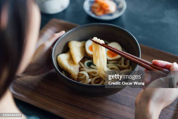 woman eating a bowl of traditional vegetarian japanese udon noodles - udon noodle stock pictures, royalty-free photos & images