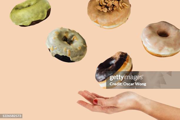 woman hand catching donuts flying on a pink coloured background - glazed food stock pictures, royalty-free photos & images