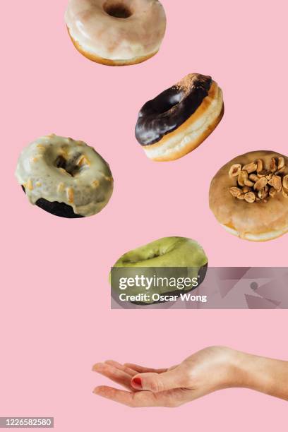 woman hand catching donuts flying on a pink coloured background - catching food stock pictures, royalty-free photos & images
