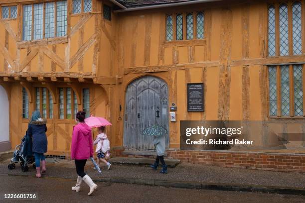 Schoolchildren and mothers walk in the rain past the medieval Little Hall in Lavenham, on 9th July 2020, in wool town Lavenham, Suffolk, England....