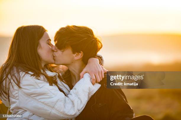 back lit teenage couple kissing outdoors at sunset - teenage couple stock pictures, royalty-free photos & images