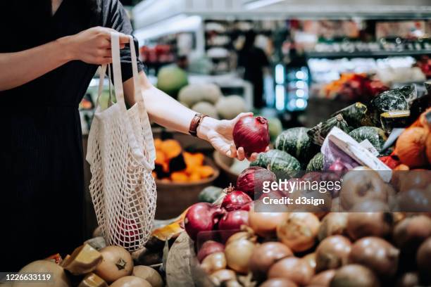 cropped shot of young asian woman shopping for fresh organic groceries in supermarket. she is shopping with a cotton mesh eco bag and carries a variety of fruits and vegetables. zero waste concept - lök bildbanksfoton och bilder
