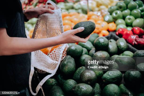 cropped shot of young asian woman shopping for fresh organic groceries in supermarket. she is shopping with a cotton mesh eco bag and carries a variety of fruits and vegetables. zero waste concept - avocado stockfoto's en -beelden