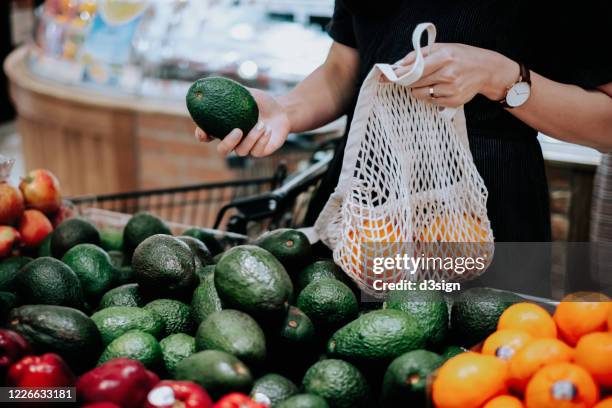 cropped shot of young asian woman shopping for fresh organic groceries in supermarket. she is shopping with a cotton mesh eco bag and carries a variety of fruits and vegetables. zero waste concept - mercado espaço de venda no varejo - fotografias e filmes do acervo