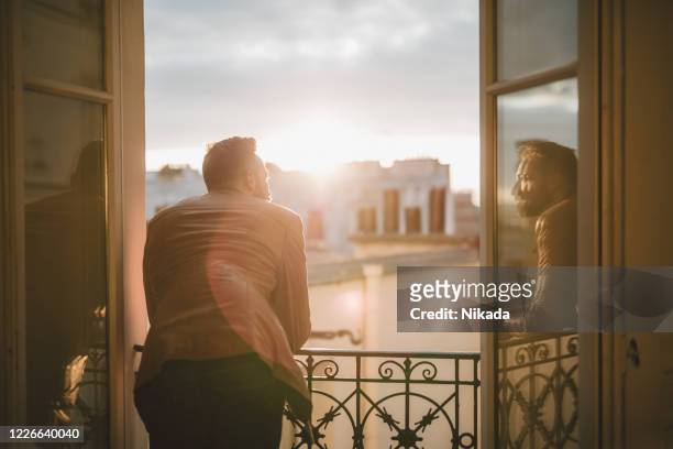 bärtiger mann, blick über die stadt bei sonnenaufgang - man looking out of window stock-fotos und bilder