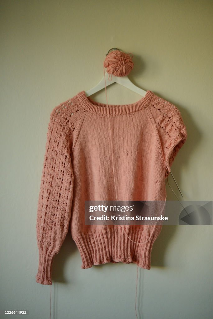Knitted sweater in peach color with one sleeve finished, another in progress
