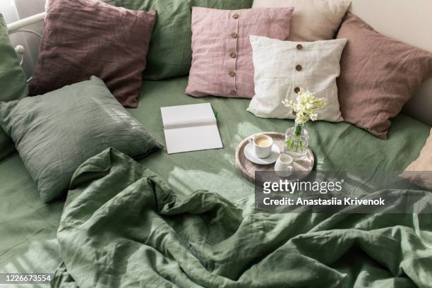 bedroom interior with bright green linen and pink cushions on bed.
from above of natural organic linen bedclothes with pillows in cozy simple bedroom with book, coffee and simple flowers on marble tray. morning concept. - bedclothes fotografías e imágenes de stock
