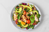 Salad with grilled chicken breast, avocado, pomegranate seeds and tomato on white background. Top view