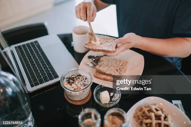 an asian chinese mid adult having breakfast in dining room while using laptop to reply emails in the morning - butter knife stock pictures, royalty-free photos & images