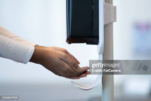 medical professional using a touchless sanitizer dispenser - desinfetar imagens e fotografias de stock